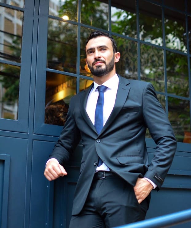 Leonardo Carvalho Tenório de terno e gravata azul, em frente a uma porta de vidro